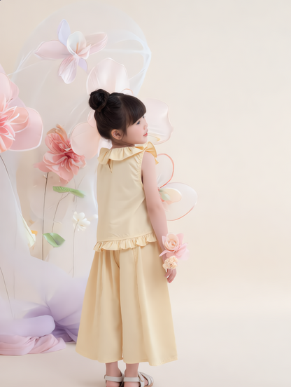Young girl in a yellow dress standing in front of decorative flowers and balloons on a light background