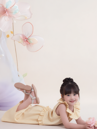 Young girl in a yellow dress lying on a white surface with decorative flowers in the background